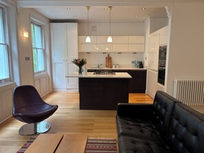 Une cuisine moderne dotée d’un îlot central, de luminaires suspendus et d’un coin repas avec un canapé et un fauteuil.