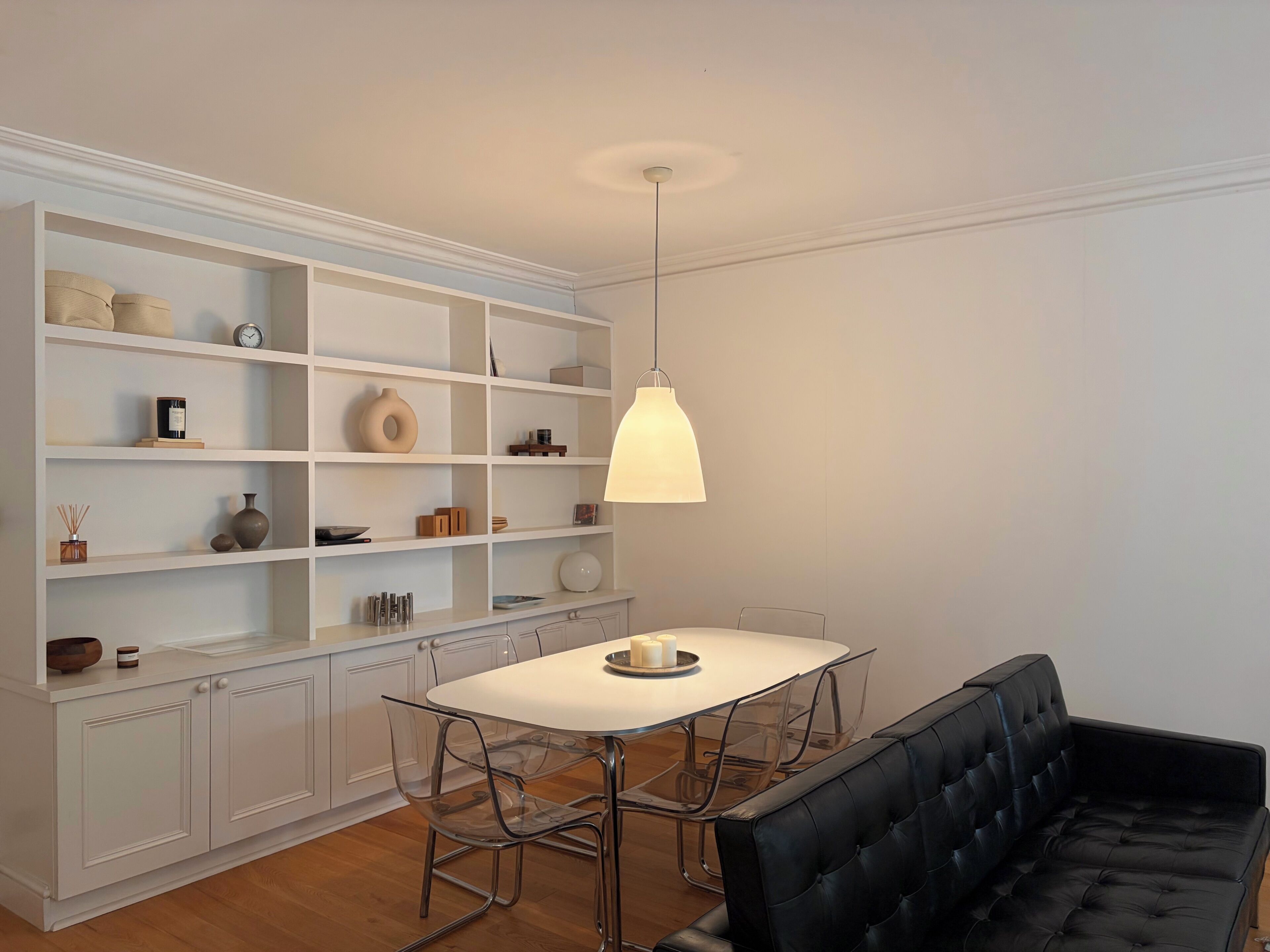 A dining area with a white table and chairs, a black cushioned bench, and a white shelving unit with various items.