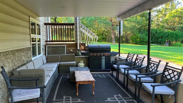 An outdoor patio with a grill, seating, and a view of the yard.