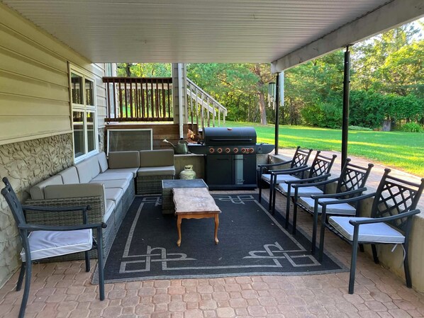 An outdoor patio with a grill, seating, and a view of the yard.