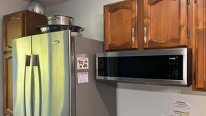 A stainless steel refrigerator with a microwave above it, wooden cabinets, and a note about recycling bins.