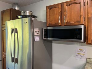 A stainless steel refrigerator with a microwave above it, wooden cabinets, and a note about recycling bins.
