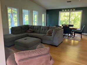A modern living room with a sectional sofa, a dining table with chairs, and large windows. - Lovstrom Estates - Beautiful Private Countryside retreat (NESBITT)