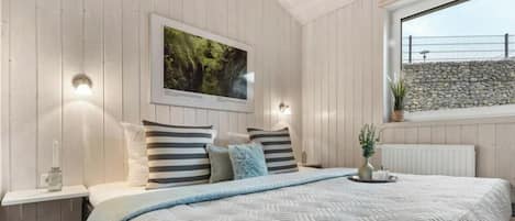 Un dormitorio con una cama, un cuadro enmarcado en la pared y una ventana con vista a un muro de piedra.
