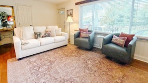A living room with a white sofa, two armchairs, a floor lamp, and a ceiling fan. - Hearth & Willow Cottage Steps from Downtown (De Soto)