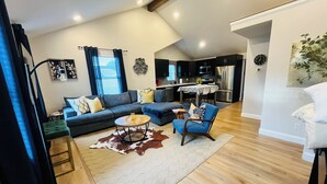 A modern living room with a sectional sofa, a blue armchair, and a wooden coffee table. - Modern Magnolia on McAdoo bungalow near Cleveland Park/Downtown GVL 3 bdrm/2 ba (Greenville)