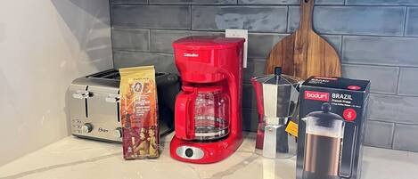 Una encimera de cocina con una cafetera roja, una prensa francesa, un tostador y un paquete de café.