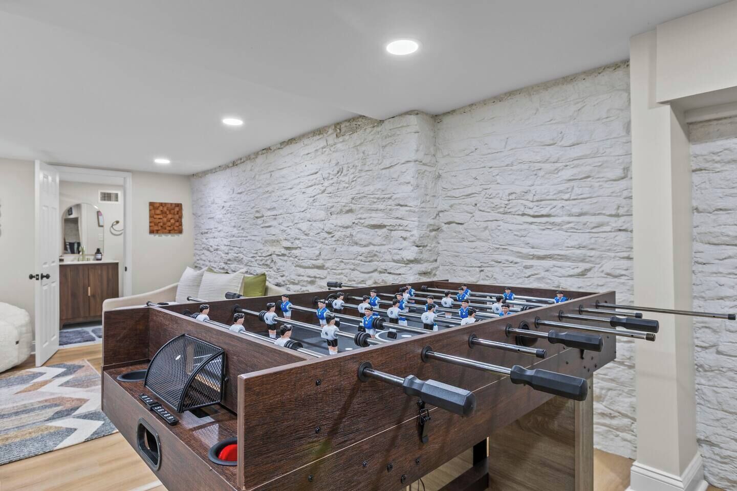 Una mesa de fútbol de mesa en una habitación con pared de piedra y puerta que da a un baño.