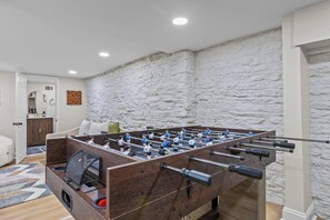 Taula de futbolí a una habitació amb paret de pedra i porta que dona a un bany.