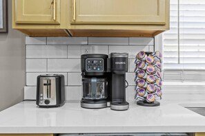 Una encimera de cocina con un tostador, una cafetera y un soporte para cápsulas de café.
