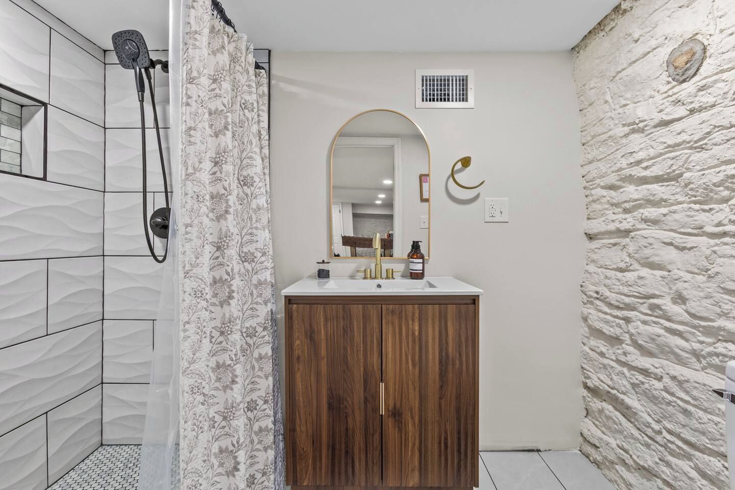Een badkamer met een douche, een wastafel met spiegel en een wand met structuur.