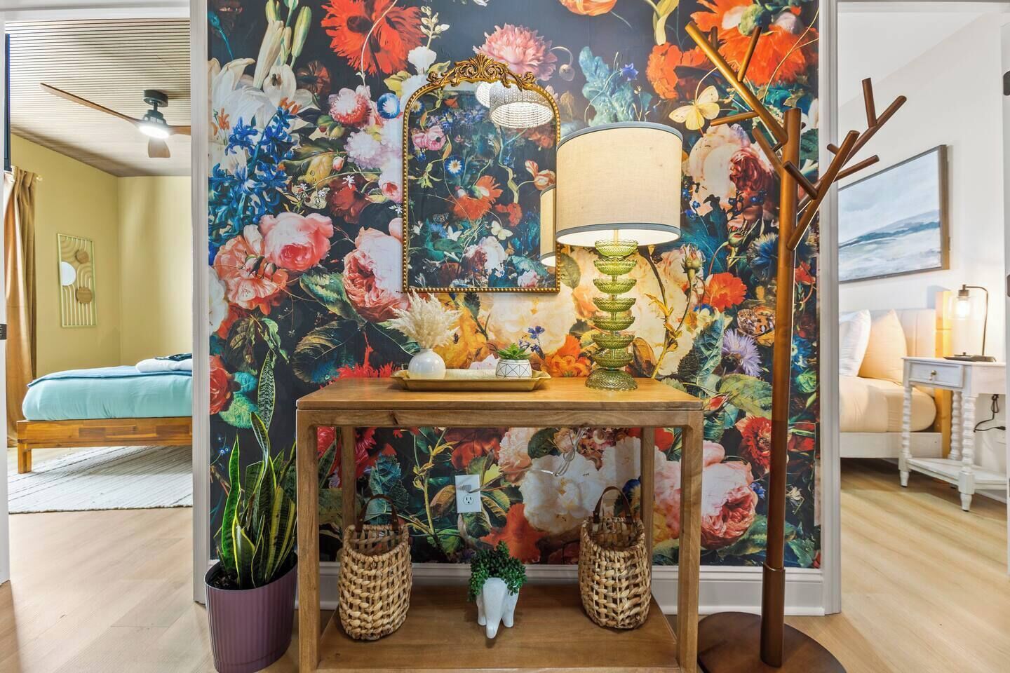 Quarto com papel de parede floral, mesa de madeira com luminária e cama com colcha azul.