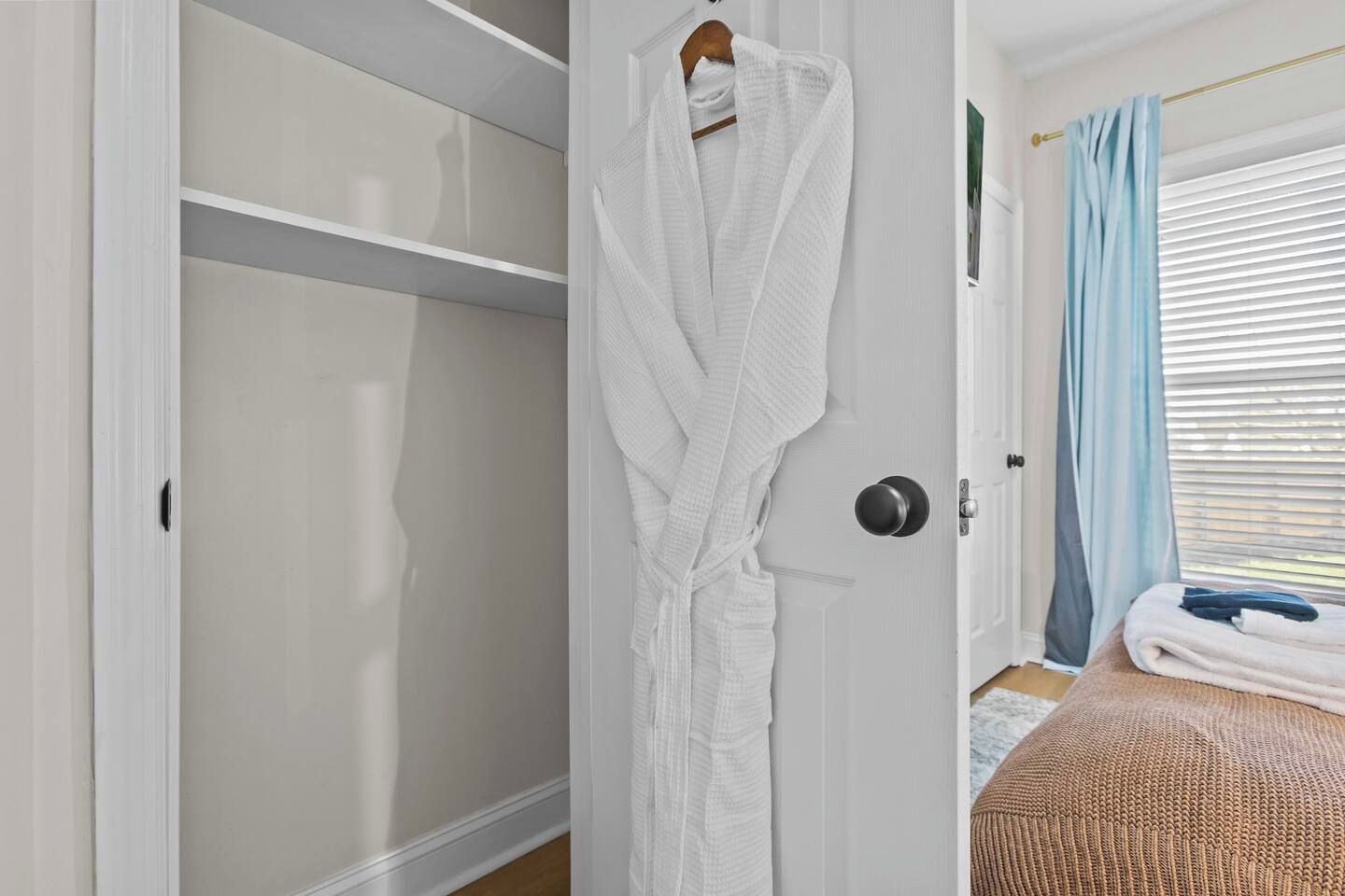 Quarto com um guarda-roupa branco, cama com cobertura marrom e janela com cortinas azuis.