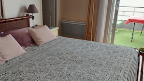 Quarto de hotel com cama, janela com cortinas, radiador e vista para área externa com mesa vermelha.