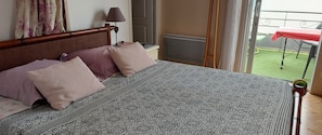 A hotel room with a bed, a window with curtains, a radiator, and a view of an outdoor area with a red table. - Bed and Breakfast 'Chambre 1' with Private Terrace and Wi-Fi (Les Sables-d'Olonne)