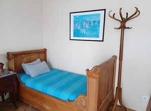Een houten bed met een blauwe spreidek en een schilderij met zeilboten, plus een kapstok.