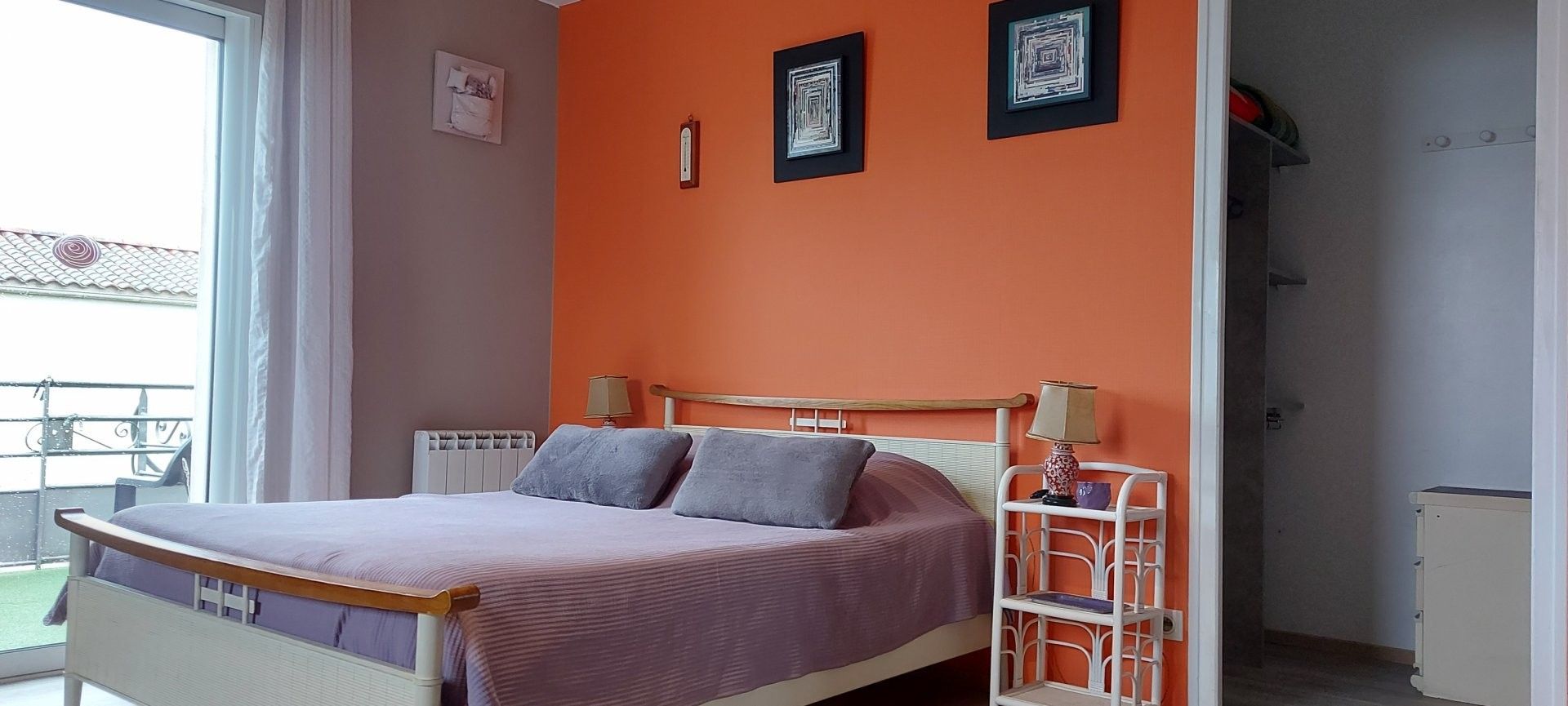 Une chambre à coucher avec un lit, deux lampes de chevet, un radiateur et une fenêtre donnant sur un balcon.