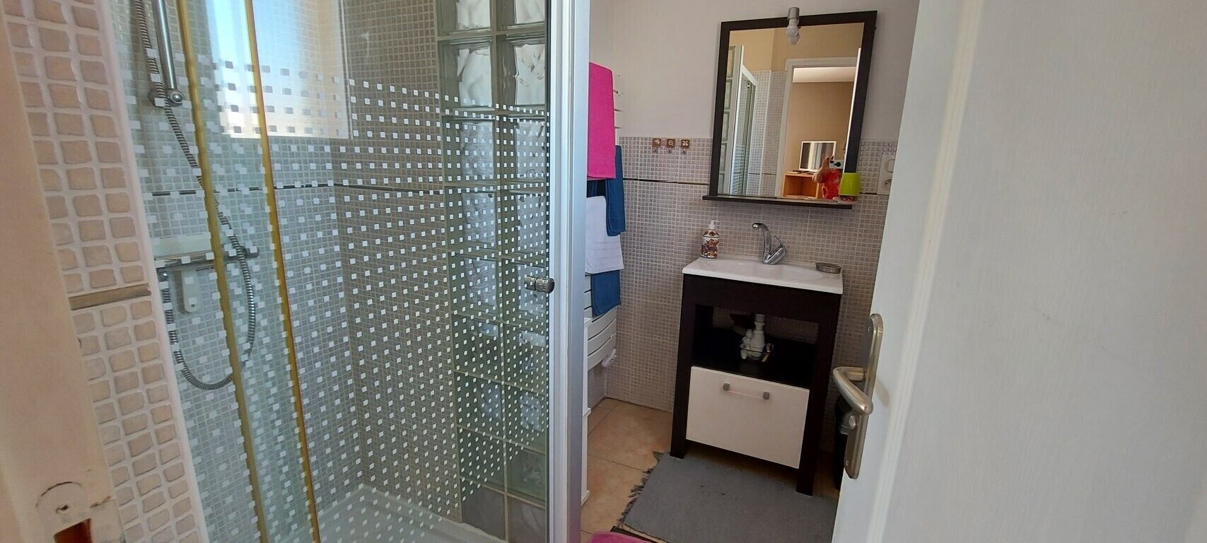 Une salle de bain avec une douche à parois de verre, un lavabo avec un miroir au-dessus et un petit meuble en dessous.
