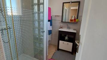Une salle de bain avec une douche à parois de verre, un lavabo avec un miroir au-dessus et un petit meuble en dessous.