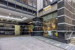 Ein modernes Gebäude mit dem Schild Adina CityLife Auckland, das eine Glasfassade und eine barrierefreie Rampe aufweist.