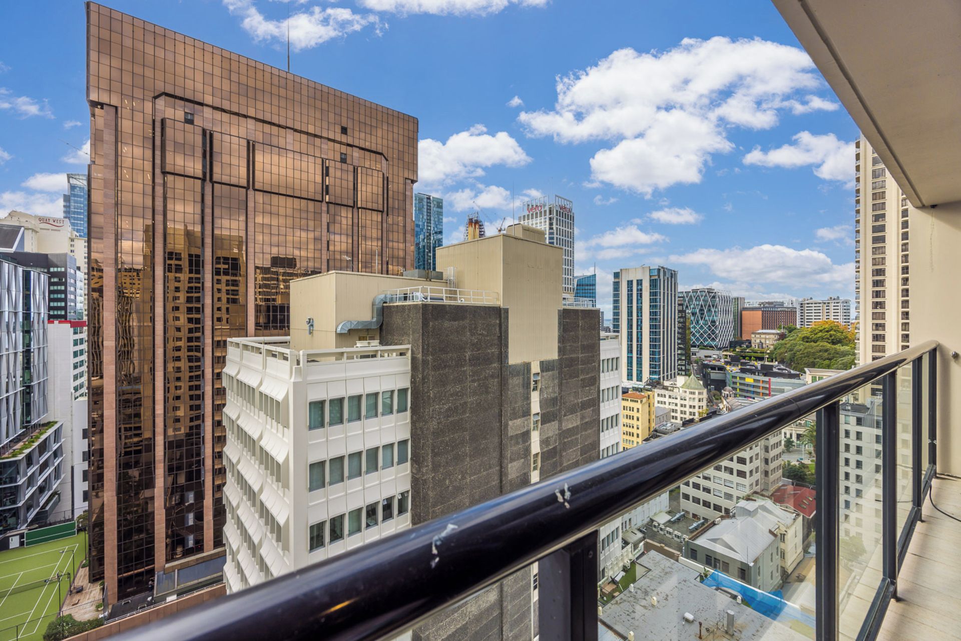 A high-rise building with a modern glass facade, surrounded by other tall buildings, viewed from a balcony.