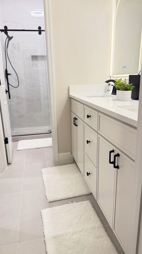 A bathroom with a shower, a white vanity with drawers, a mirror, and a potted plant. - Beautiful townhome near Celebration Point and UF Shands (Gainesville)