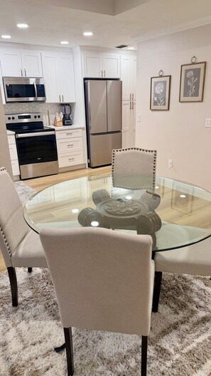 A modern kitchen with white cabinetry, stainless steel appliances, and a glass-top dining table surrounded by cushioned chairs. - Beautiful townhome near Celebration Point and UF Shands (Gainesville)