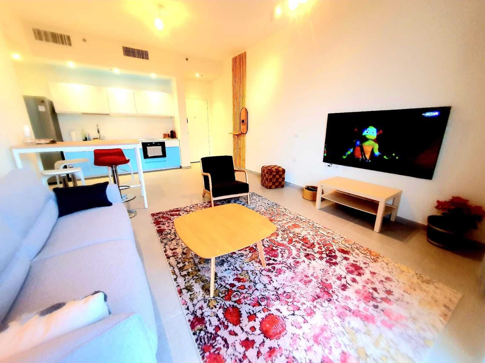 Una sala de estar moderna con un sofá, una mesa de centro, un televisor y una cocina al fondo.