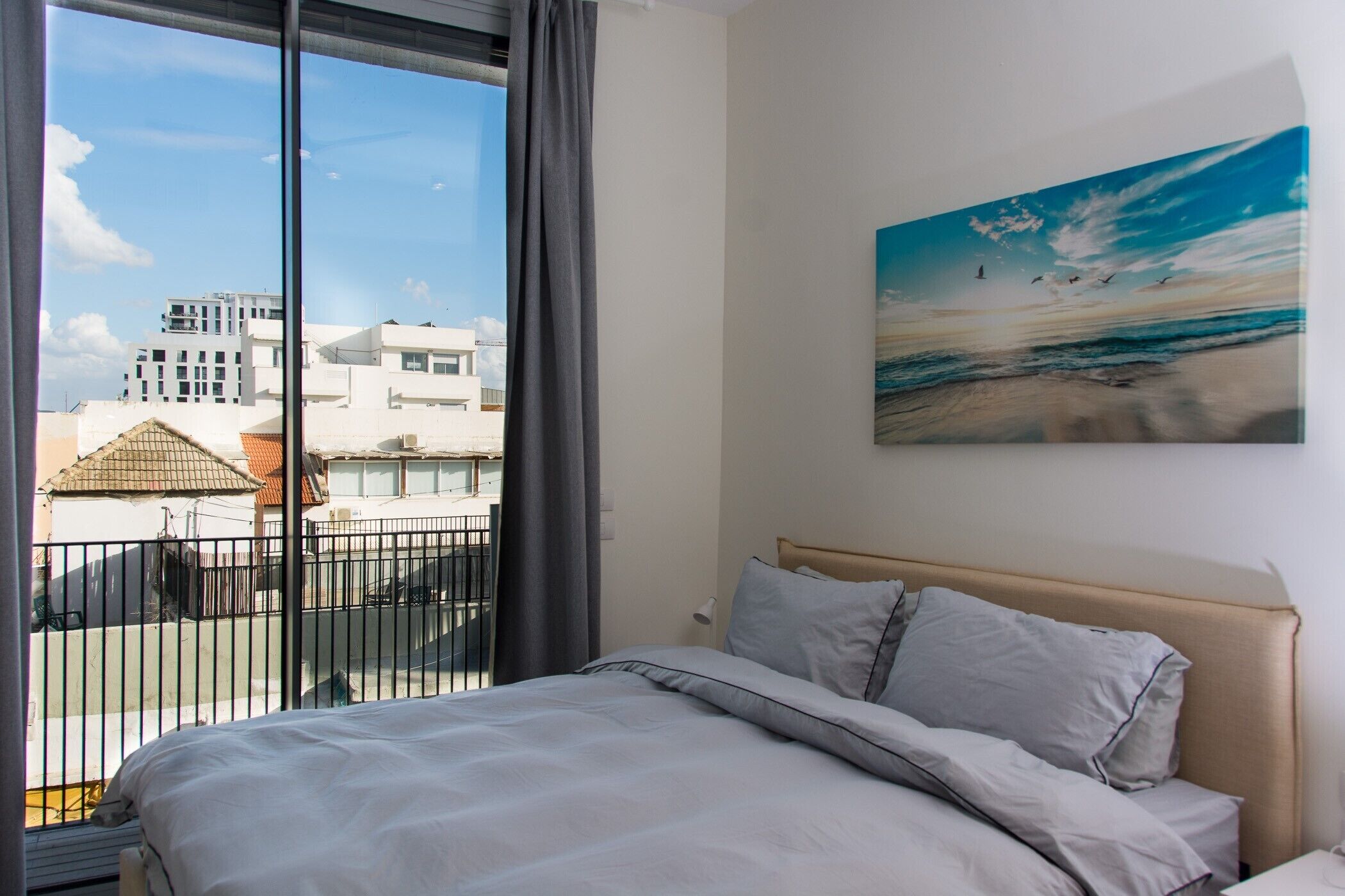 A hotel room with a large bed, a painting of birds on the wall, and a view of buildings through the window.