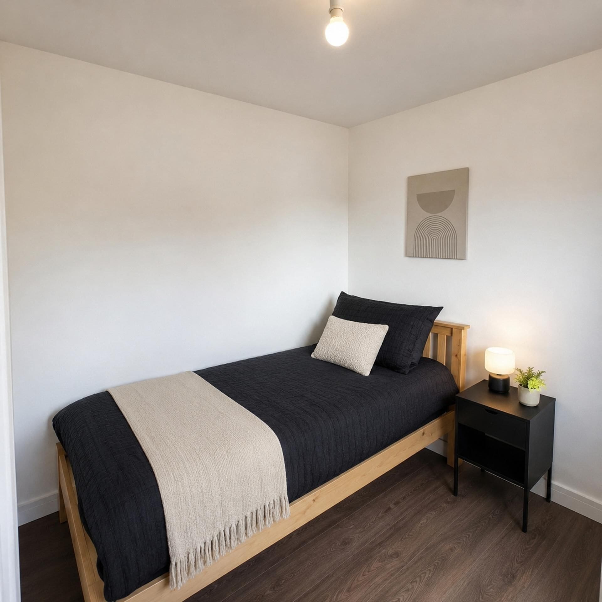 A bedroom with a bed, bedside table, lamp, and a wall-mounted artwork.