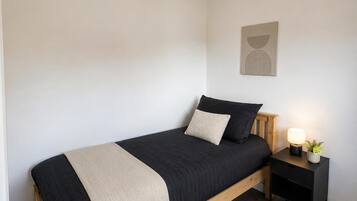A bedroom with a bed, bedside table, lamp, and a wall-mounted artwork.