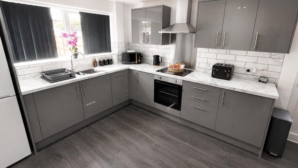 A modern kitchen with grey cabinets, a built-in oven, a microwave, and a toaster. - The Cozy Home - Cozy 3 Bedroom House (Telford)