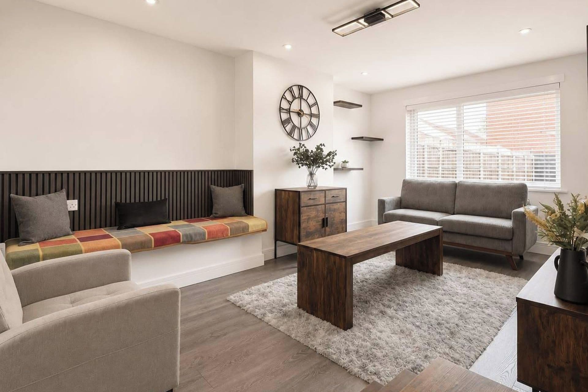 Una sala moderna con un sofá, una mesa de centro, una mesita auxiliar y un ventanal con persianas.