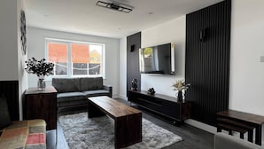 A modern living room with a sofa, coffee table, and TV against a wall. - The Cozy Home - Cozy 3 Bedroom House (Telford)
