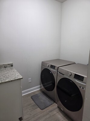 A laundry room with two front-loading washing machines, a granite countertop, and a gray rug.