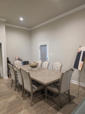 Une salle à manger avec une grande table rectangulaire, six chaises rembourrées et un vase décoratif posé sur la table.