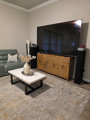 Un salon équipé d’un téléviseur à écran plat, d’un meuble en bois, d’un canapé vert et d’une table basse sur laquelle est posé un vase.