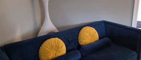A dark blue sofa with two yellow pillows and a white vase with pampas grass against a plain wall.