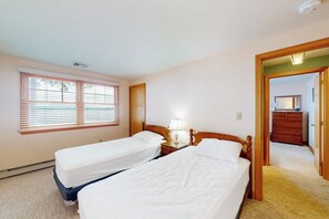 Un dormitorio con dos camas individuales, una mesita de noche con lámpara, un aparador y una ventana con persianas.