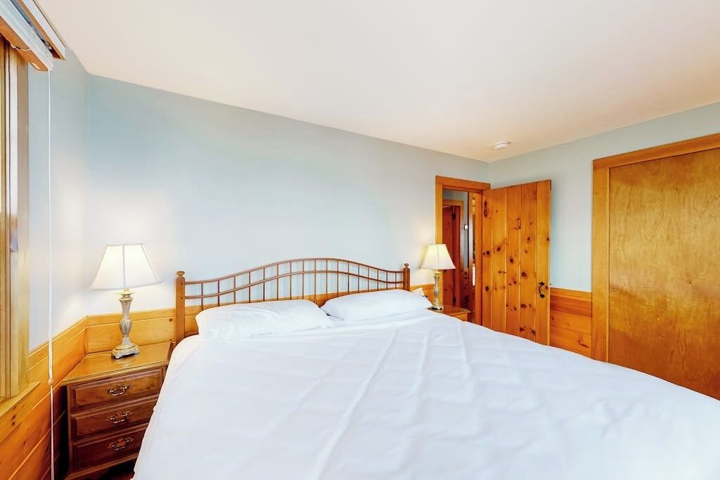 A hotel room with a wooden bed, two bedside tables with lamps, a wooden wardrobe, and a door.