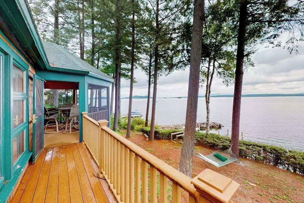 A wooden deck with a view of a lake, a covered seating area, and a hammock.