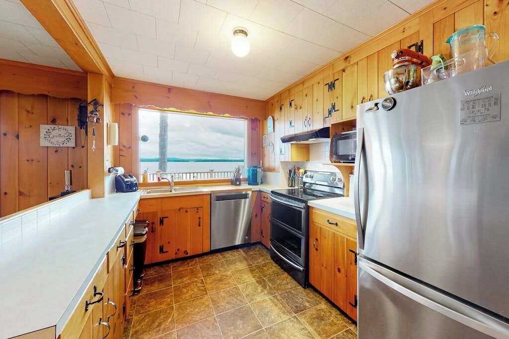 Een keuken met houten kastjes, een roestvrijstalen koelkast en een raam met uitzicht op het water.