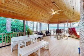 Un espacio al aire libre techado con una terraza de madera, una mesa blanca, bancos, sillas y una hamaca.