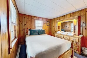 Ein Zimmer mit Holzwänden, einem Bett, einer Kommode und einem Spiegel.