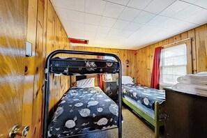 Ein Zimmer mit zwei Etagenbetten, einer Holzwand, einem Fenster mit roten Vorhängen und einem kleinen Schreibtisch mit Lampe.