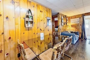Ein Zimmer mit Holzwänden, einem Glastisch und Stühlen, einem blauen Sofa und einem kleinen Regal mit Dekoration.
