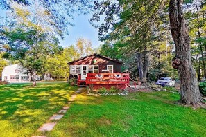 Ein kleines Holzhaus mit Veranda, umgeben von Bäumen und einem grünen Rasen.