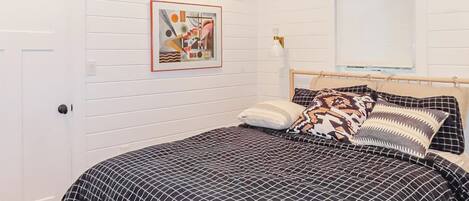 A bedroom with a bed, a wall-mounted picture, a window with blinds, and a door.