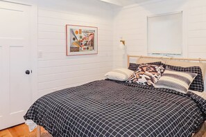 Une chambre à coucher avec un lit, un tableau accroché au mur, une fenêtre avec des stores et une porte.