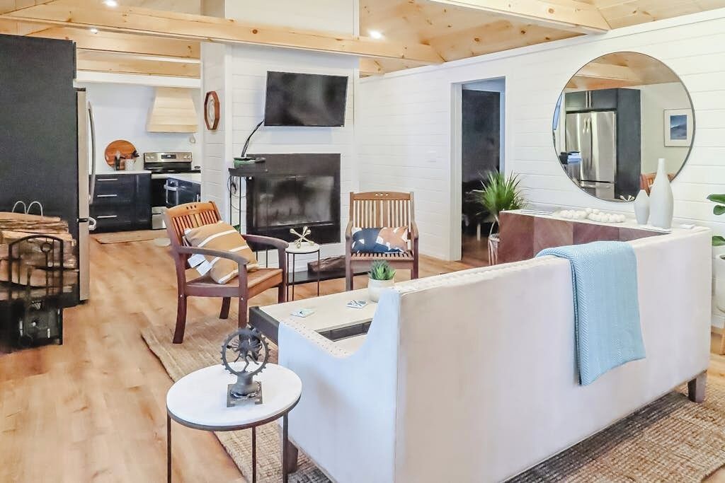 Ein modernes Wohnzimmer mit einem weißen Sofa, zwei Holzstühlen, einem kleinen Tisch mit einer Globus und einer Küchenzeile im Hintergrund.